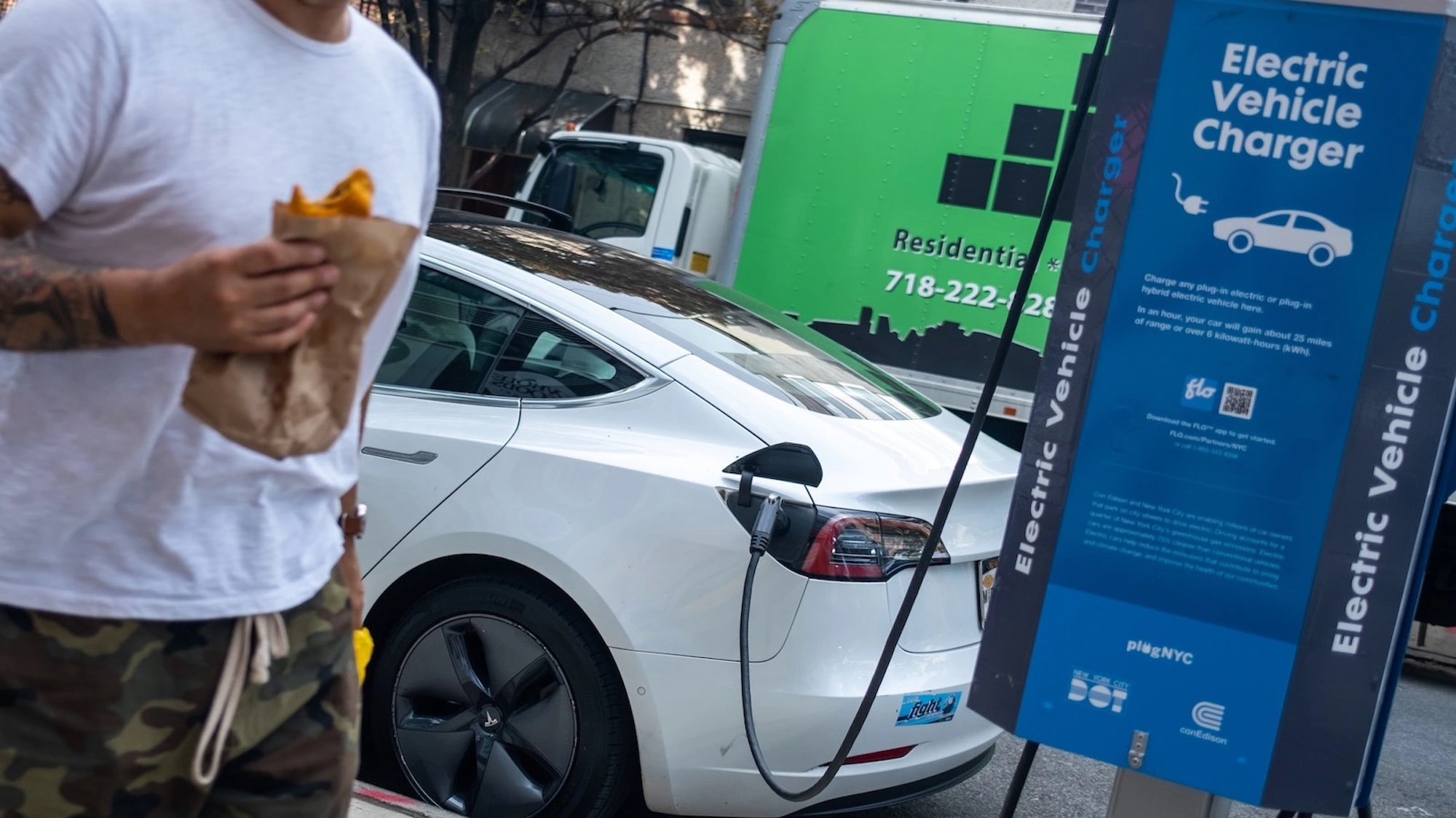 A man walking by an EV charging station with a sandwich