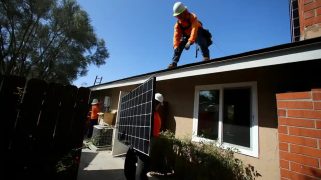 Workers lift a solar panel on to the roof of a house in San Diego, California, US.