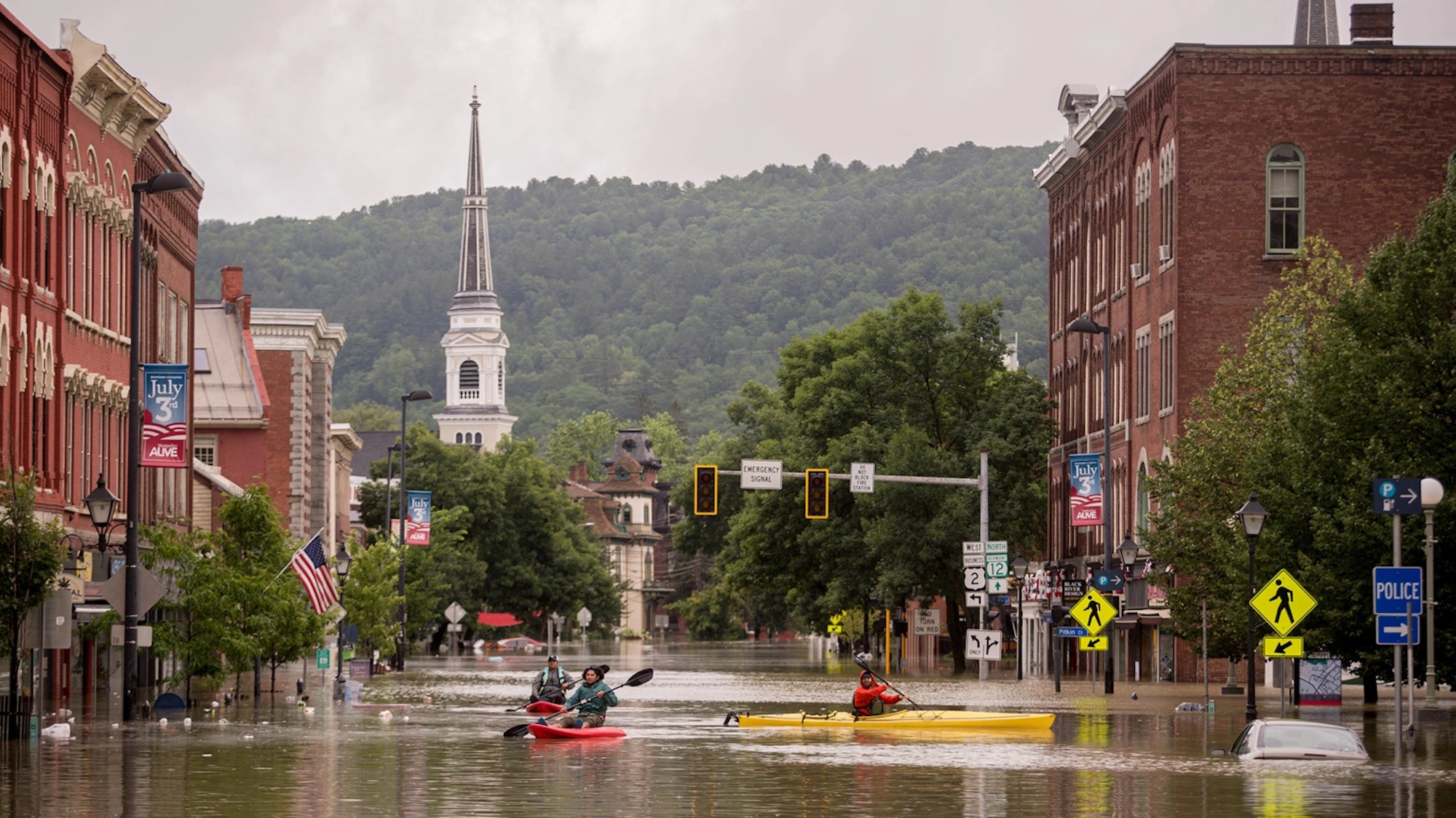 A photo of downtown Vermont, with people traveling on streets via kayak