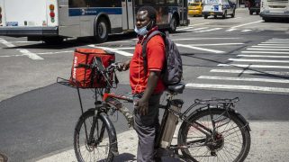 A Black man visibly sweating while delivering grubhub on his bike