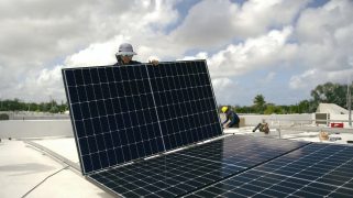 A man with light brown skin installing solar panels on the roof in PR