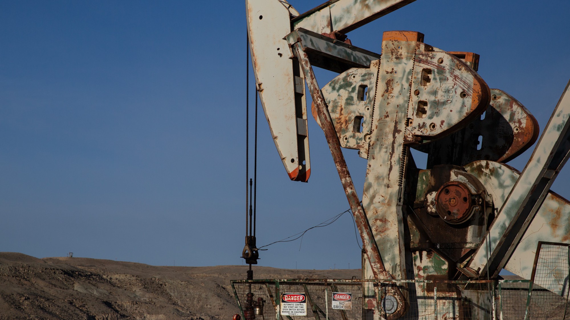 A large rusting machine sits in front of a grey desert and blue sky.