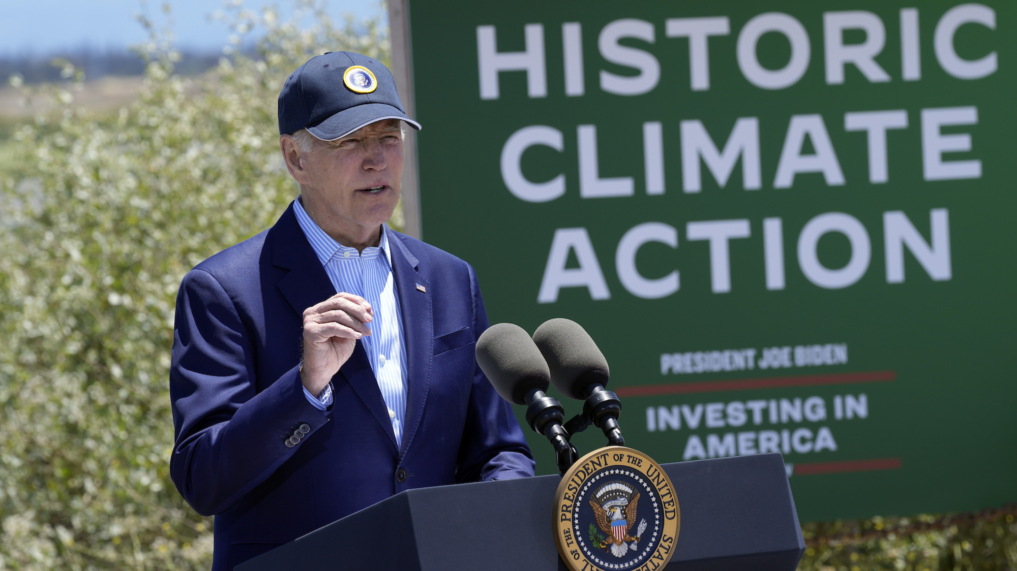 Biden speaking at a podium outside, next to a sign that says, "Historic Climate Action"