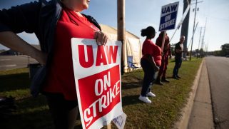 UAW members strike outside the General Motors Lansing redistribution facility in red UAW shirts and signs