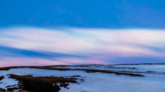 Pink and white clouds hover over a snow dappled landscape.