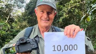 A white man with a baseball cap holds up a sign that says 10,000.