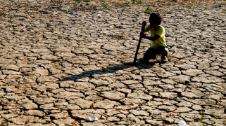 A child crouches over cracked, dry land.