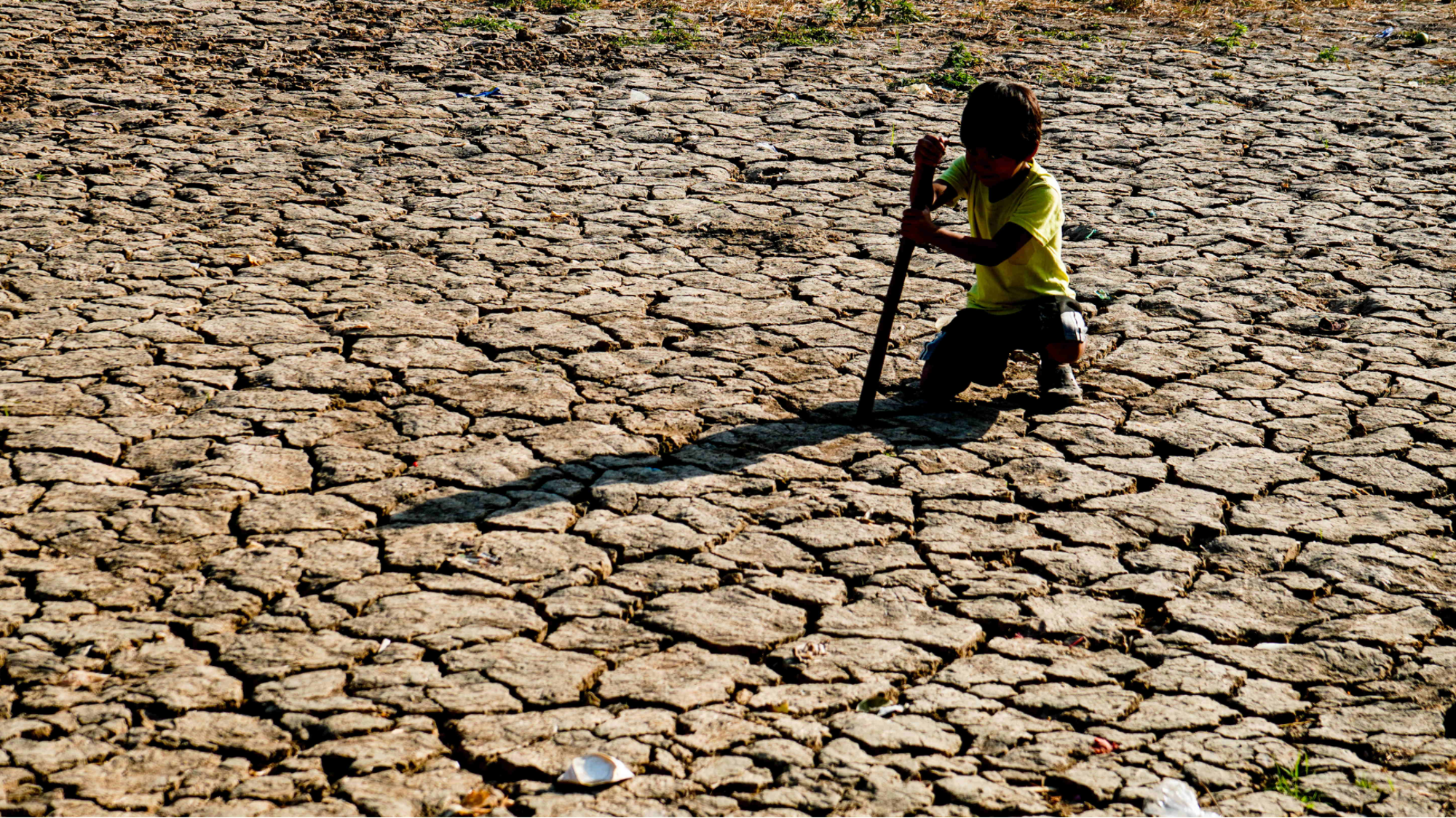 A child crouches over cracked, dry land.