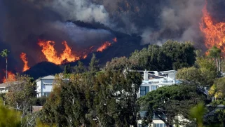 Black mountains aflame encroach on houses and green trees.