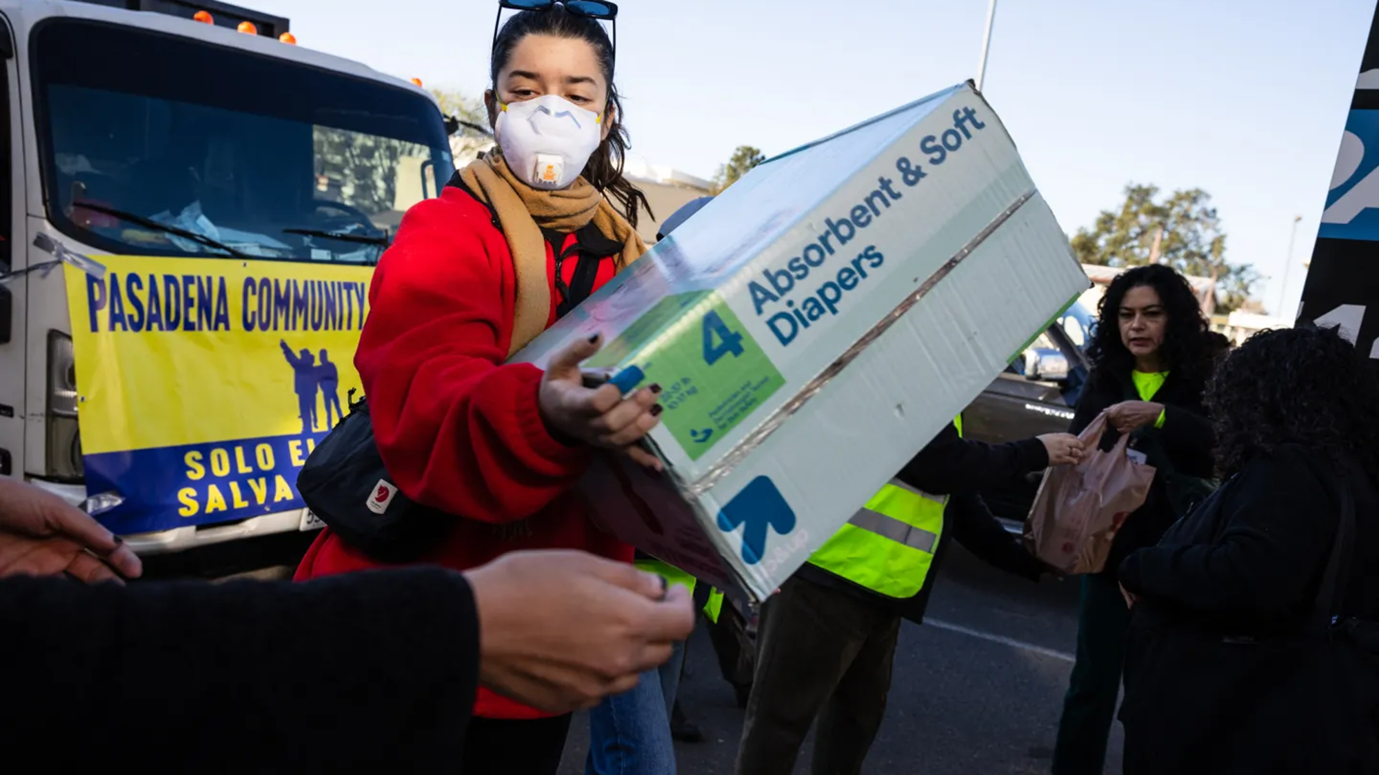 A person with a red jacket holds a box of diapers.