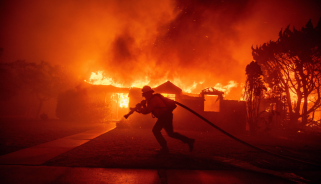 A firefighter pulls a hose through flames