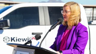 A white woman in a purple jacket speaks at a podium.