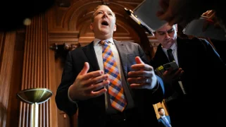 White man wearing orange tie opens his mouth wide.