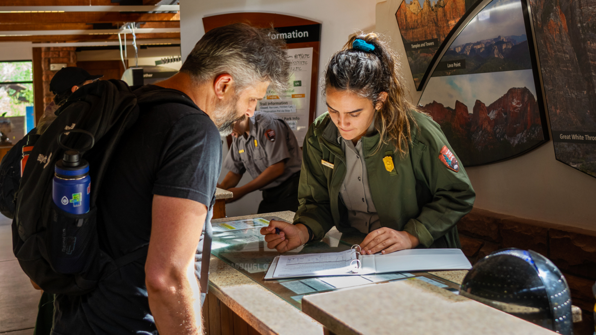 A park ranger and a hiker look at a folder on a desk.