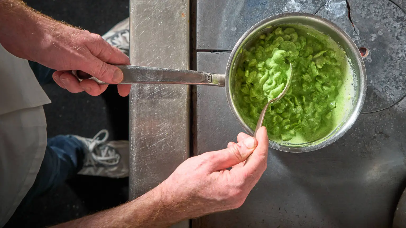 White hands stir a pot with a green substance.