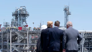 Three men in suits stand facing a metal structure.