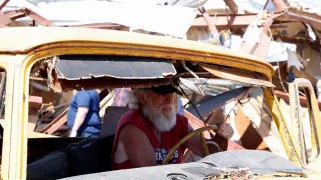 A person in a broken truck drives through debris
