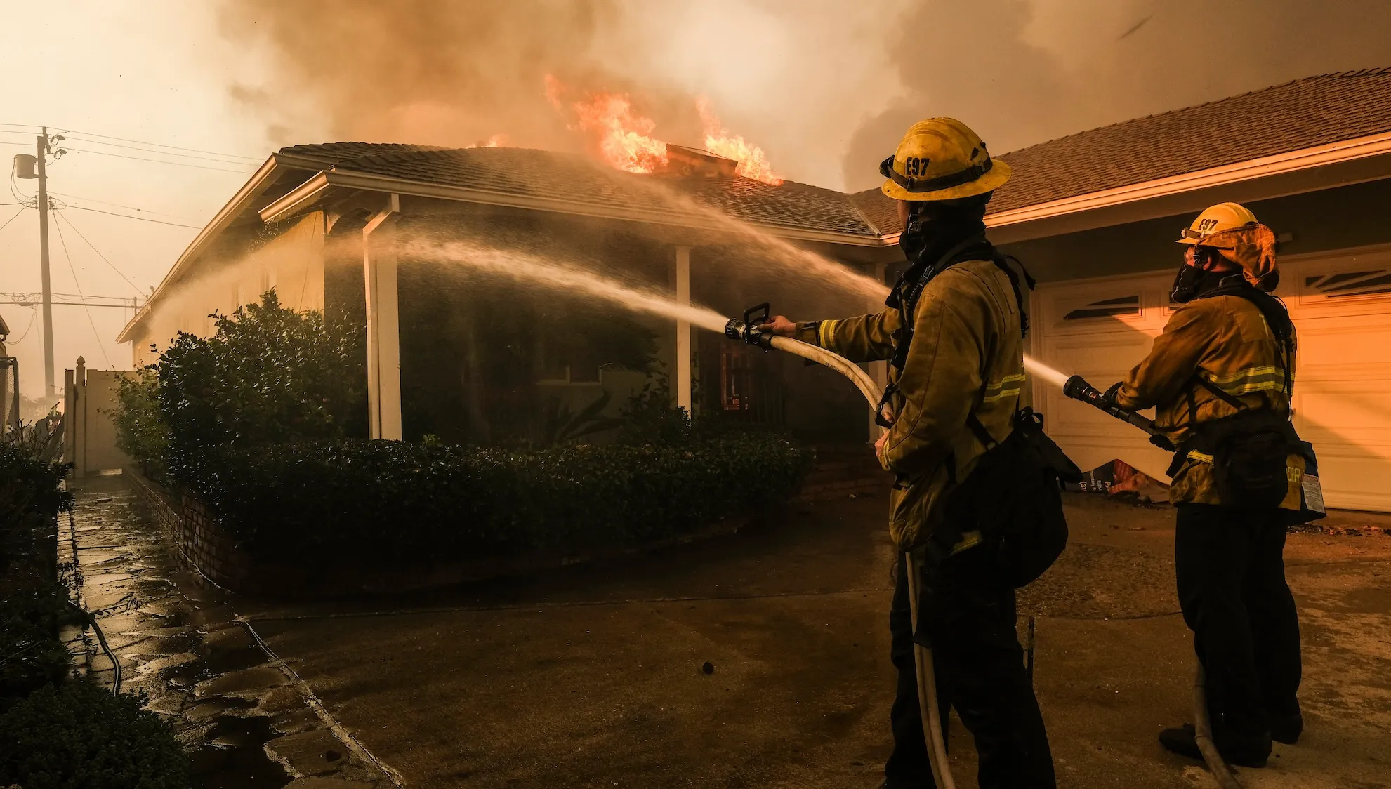 Two firefighters spray water on a burning house.