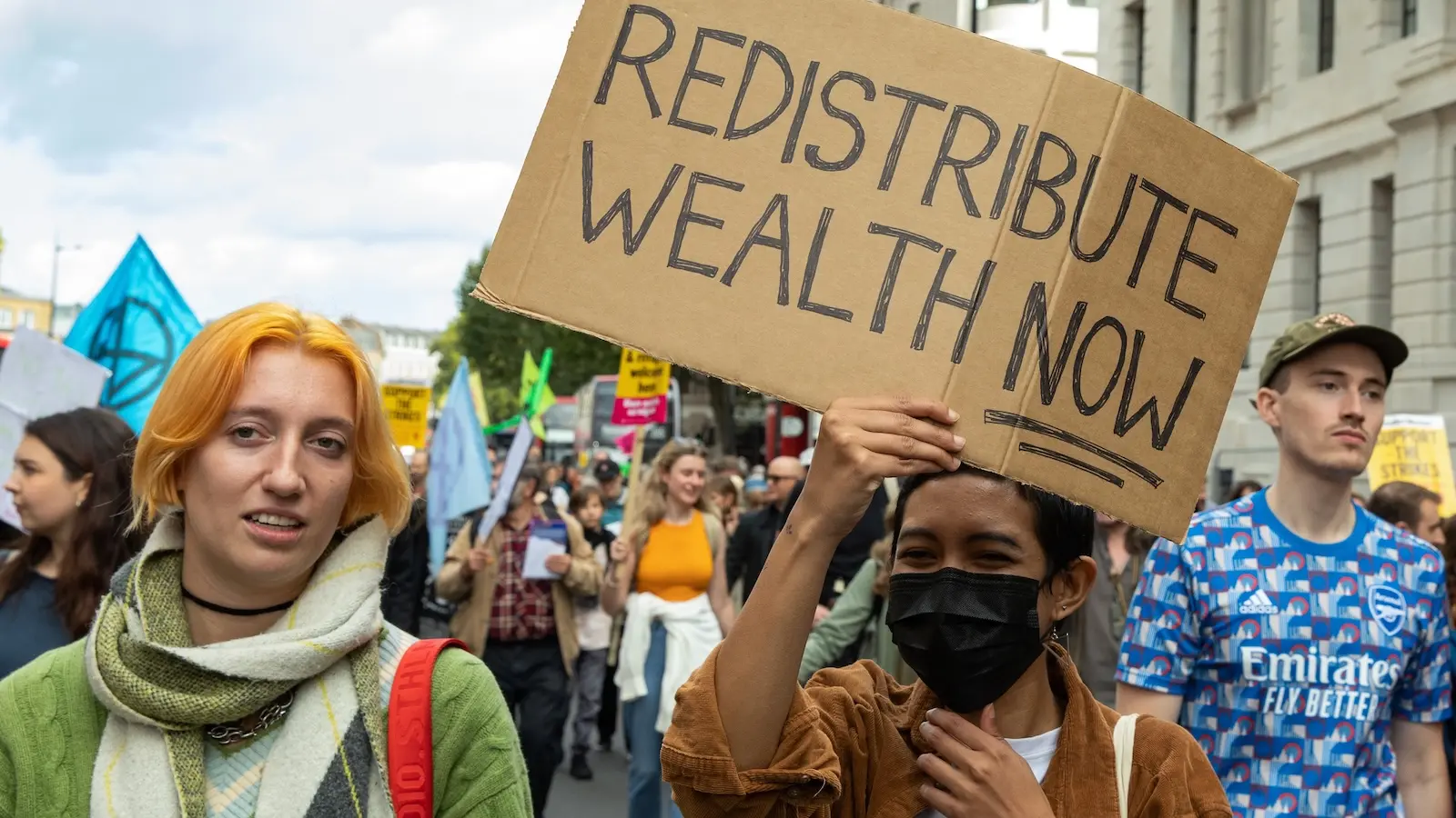 Protesters hold sign that says "redistribute wealth now"