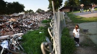 A kid stands next to a wire fence.