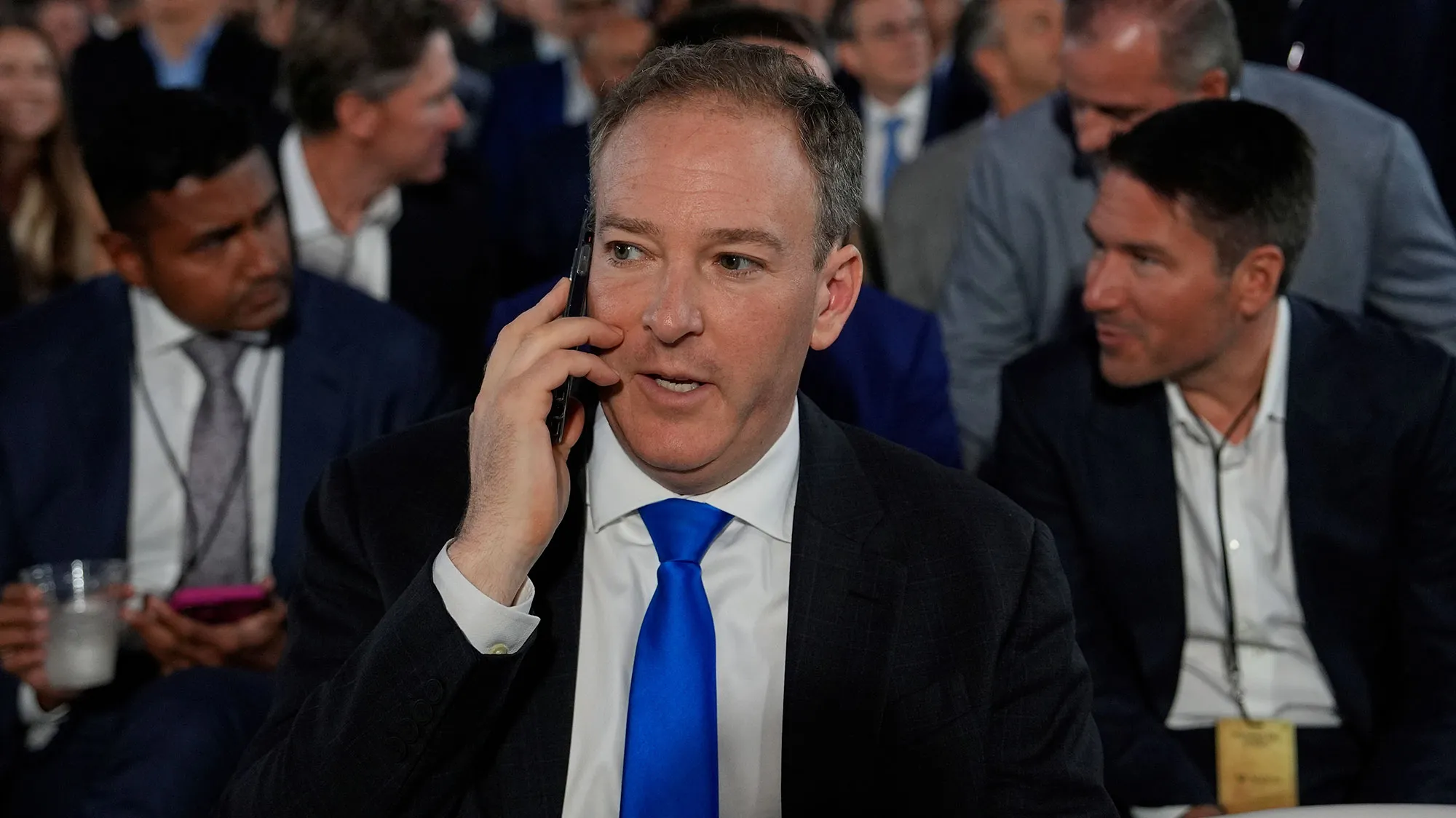 A white man with a blue tie speaks on a cell phone