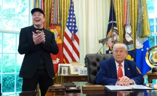 Elon Musk smiling and clapping next to Donald Trump in the oval office.