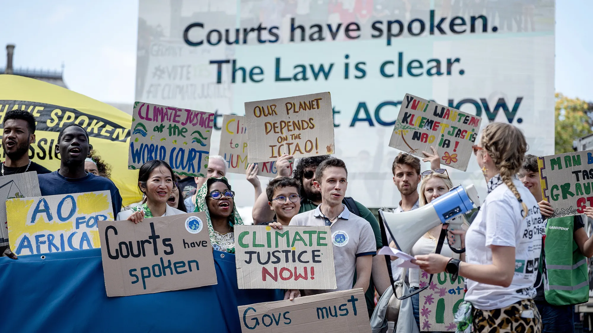 Folks holding signs saying "Climate Justice Now" "Courts have spoken Law is Clear"