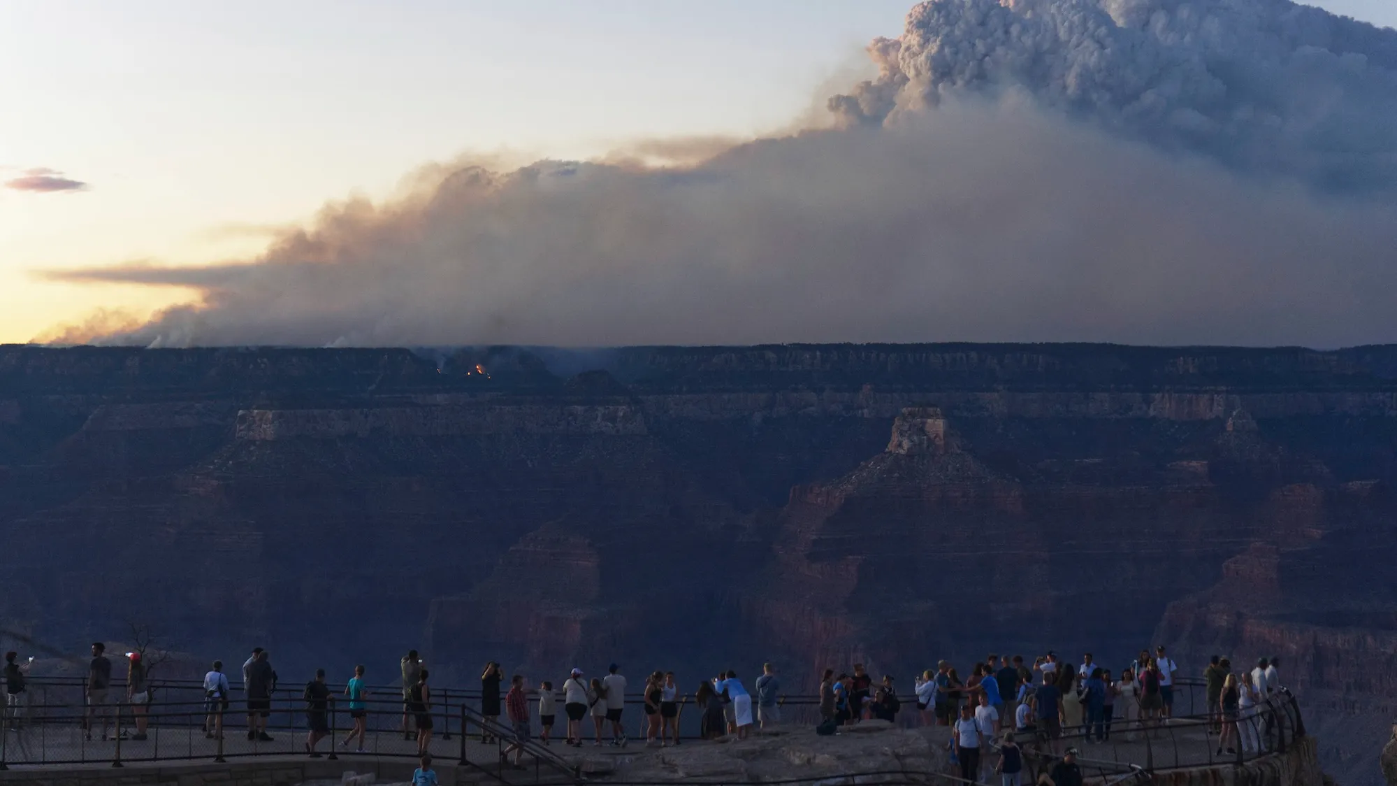 A crowd looks at a cloud of smoke over the Grand Canyon