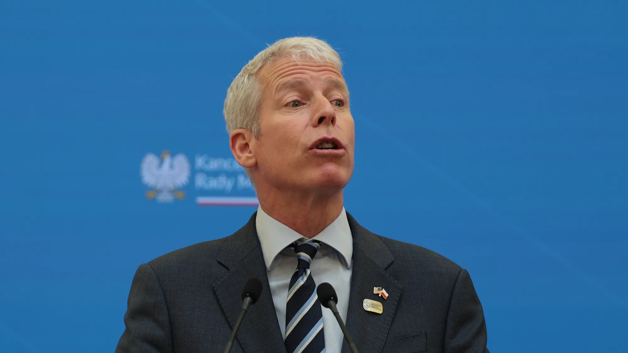 A white man in front of a blue background.