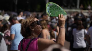 FILE - A tourist uses a fan to shade her face from the sun while waiting to watch the Changing of the Guard ceremony outside Buckingham Palace, during hot weather in London, July 18, 2022. (AP Photo/Matt Dunham, File)