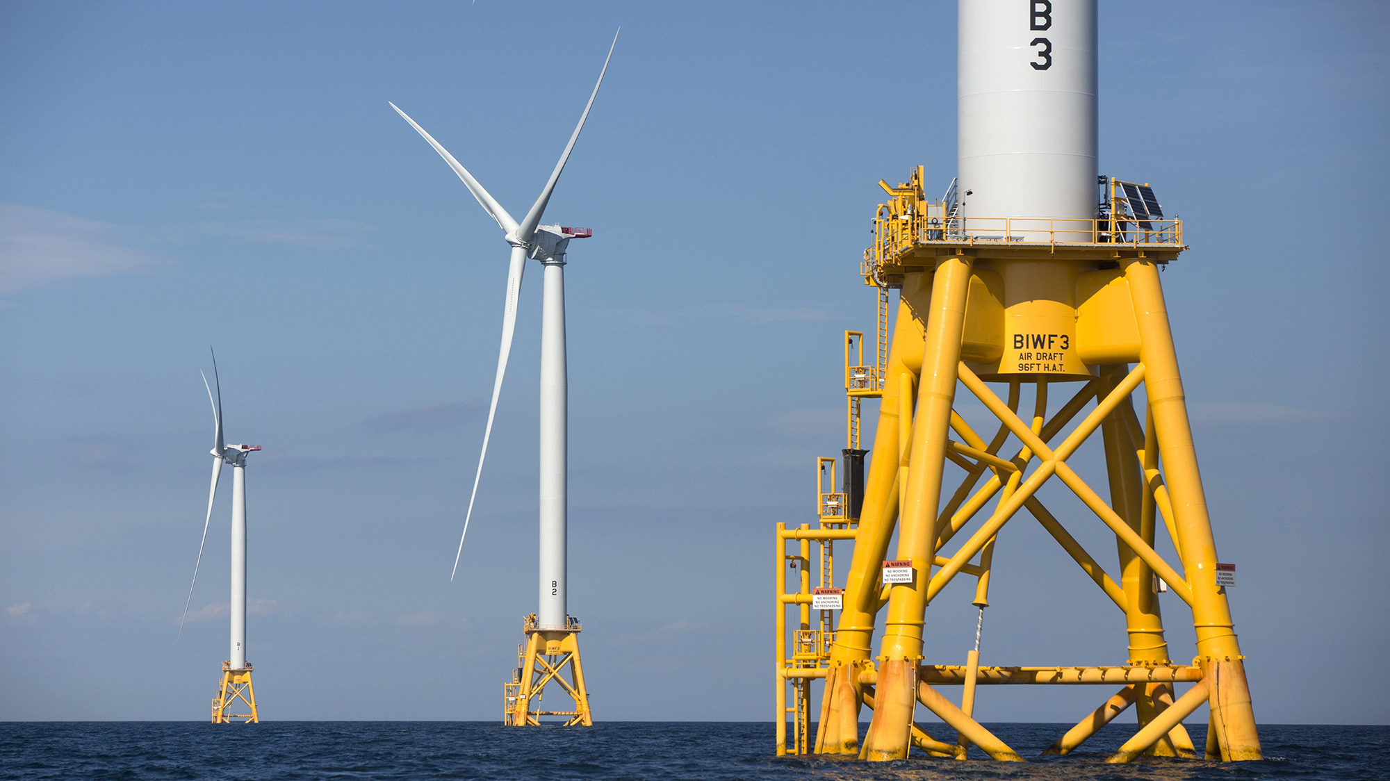 Wind turbines on the ocean mounted on yellow mounts.