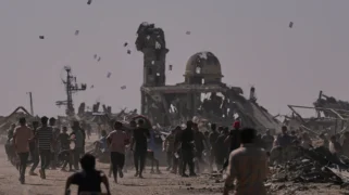 Palestinians walk through a destroyed city. Leaflets drift through a hazy sky. Palestinians collect warning leaflets dropped by an Israeli drone Palestinians walk through a destroyed city. Leaflets drift through a hazy sky.