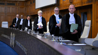 Members of the International Court of Justice stand in full regalia in front of their desk.