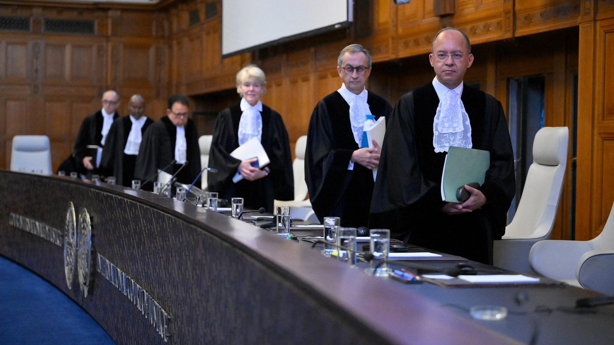 Members of the International Court of Justice stand in full regalia in front of their desk.