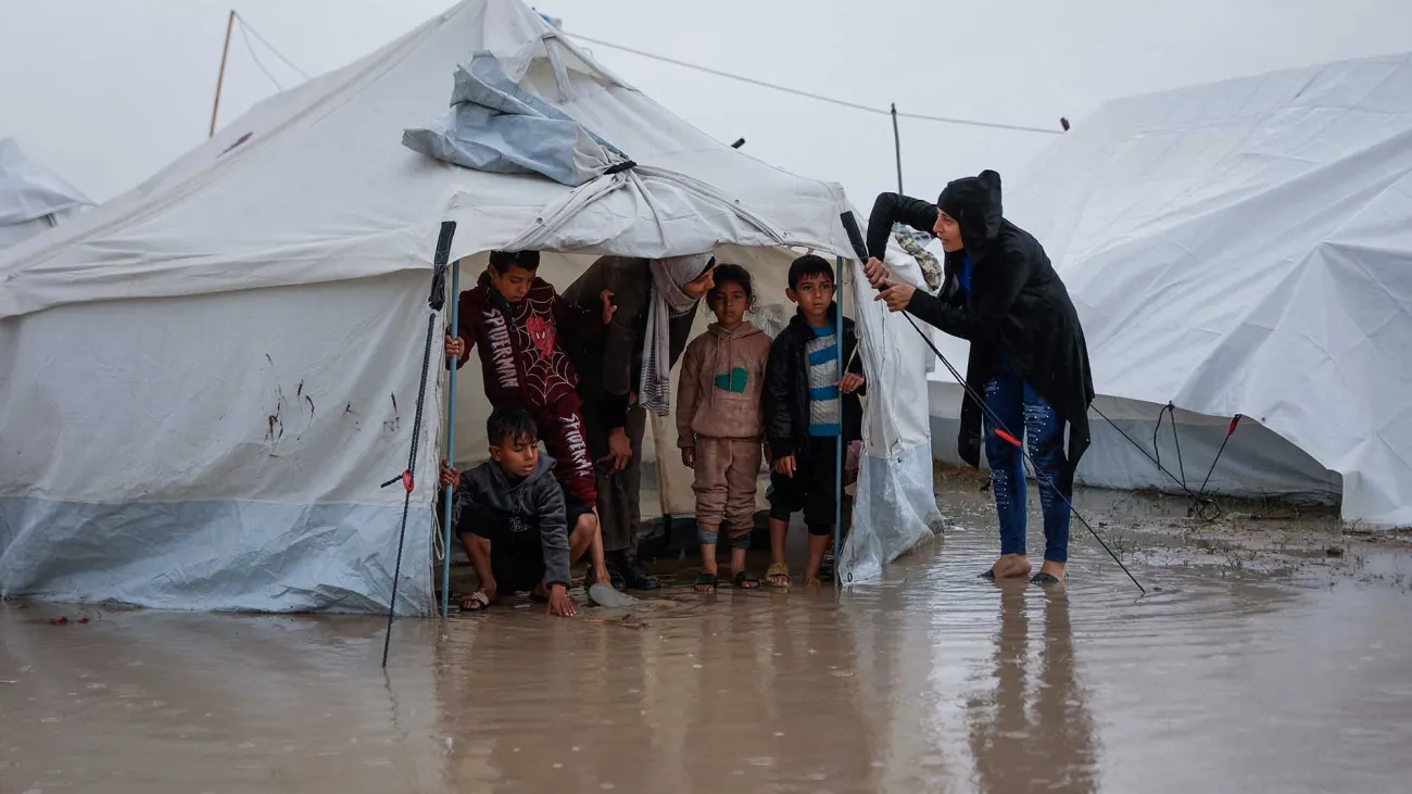 A woman fixes her tent as children stand inside at a makeshift camp.