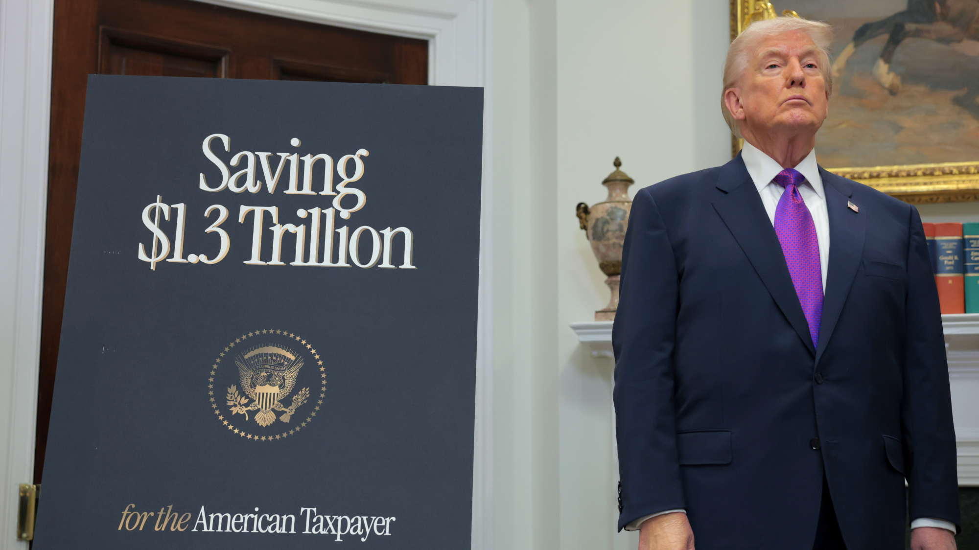 Trump stands next to a sign that says "Saving $1.3 Trillion"
